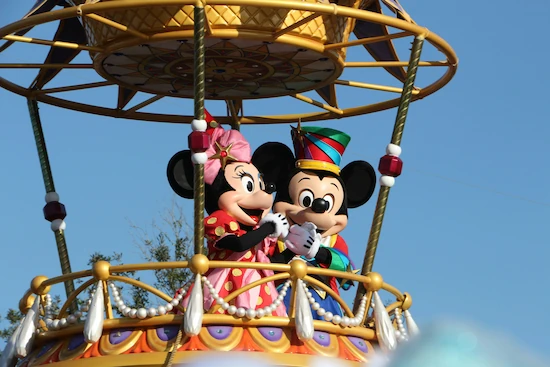 Mickey and Minnie standing together on a golden, gated, and adorned hot air balloon.