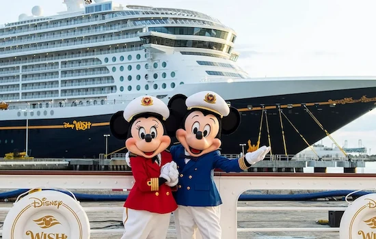 Mickey and Minnie mouse posing together in a captain's hat with a Disney cruise ship behind them in the distance.