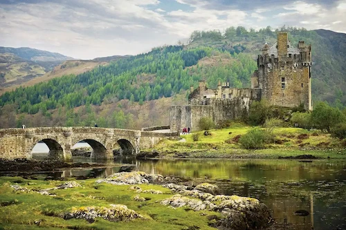 A scenic, hilly view with an old castle across a bridge.